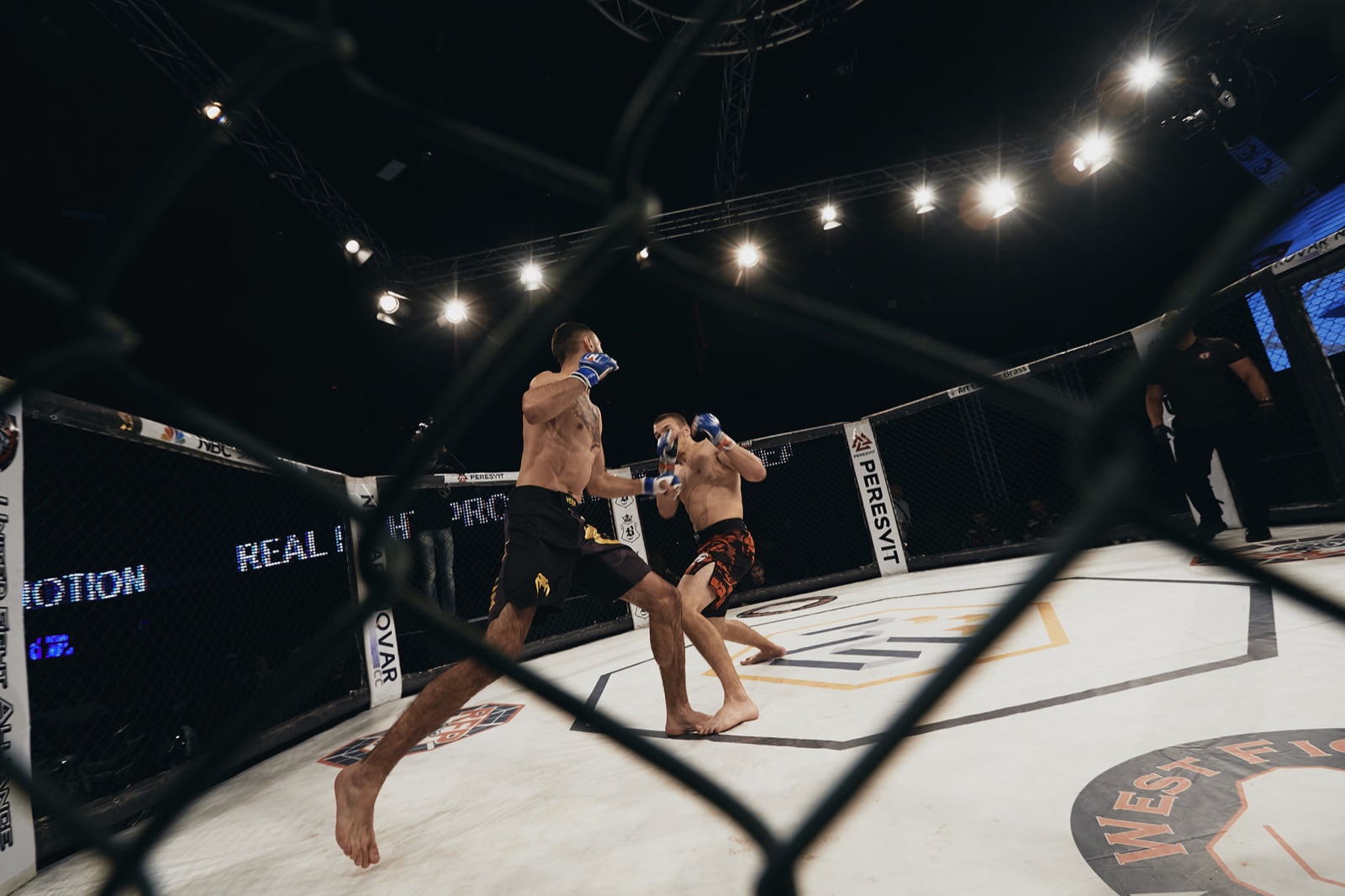 Two fighters face each other with the referee at the centre of a brightly lit cage.