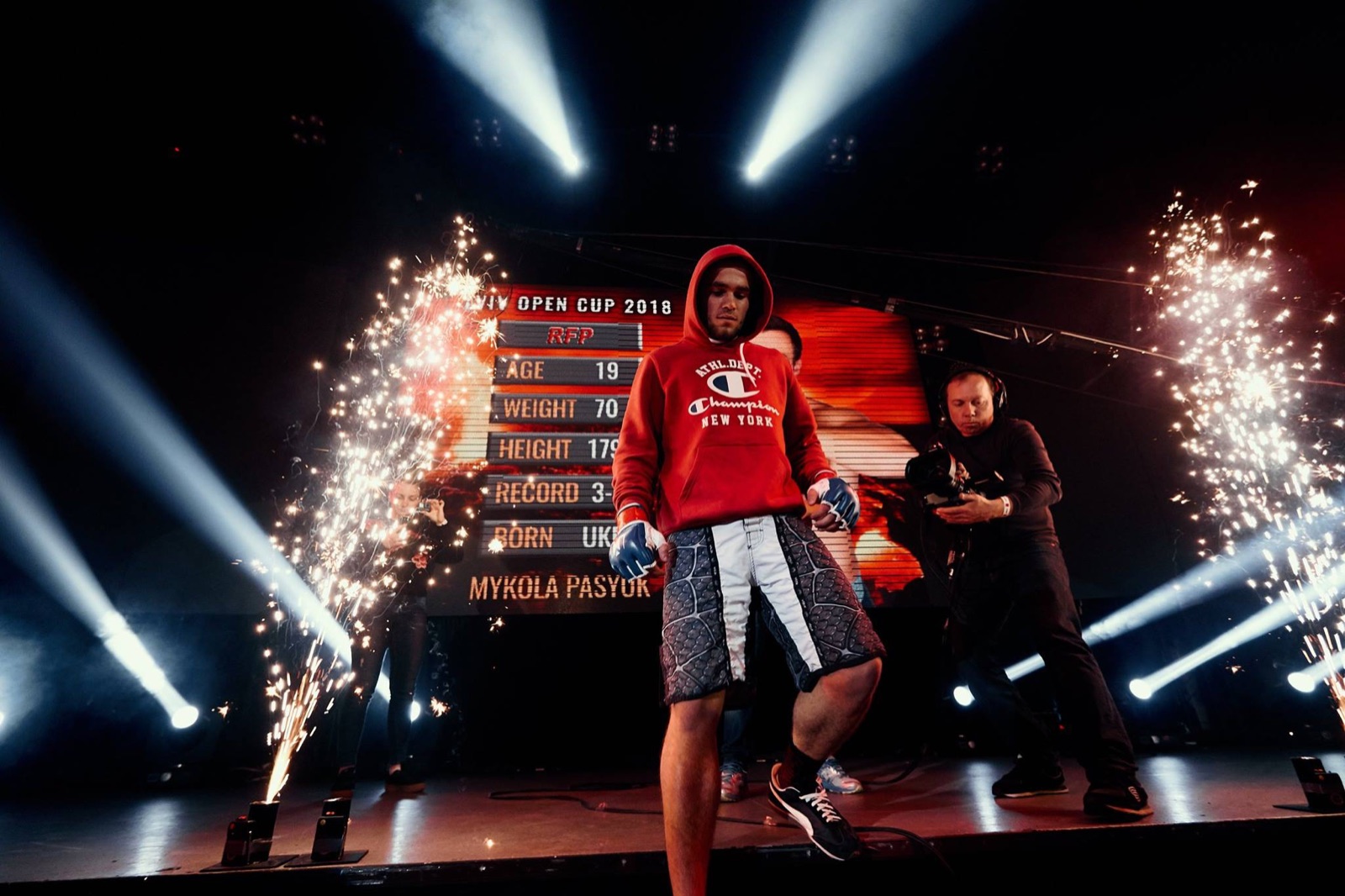 A fighter in red enters the arena between fountains of sparks.