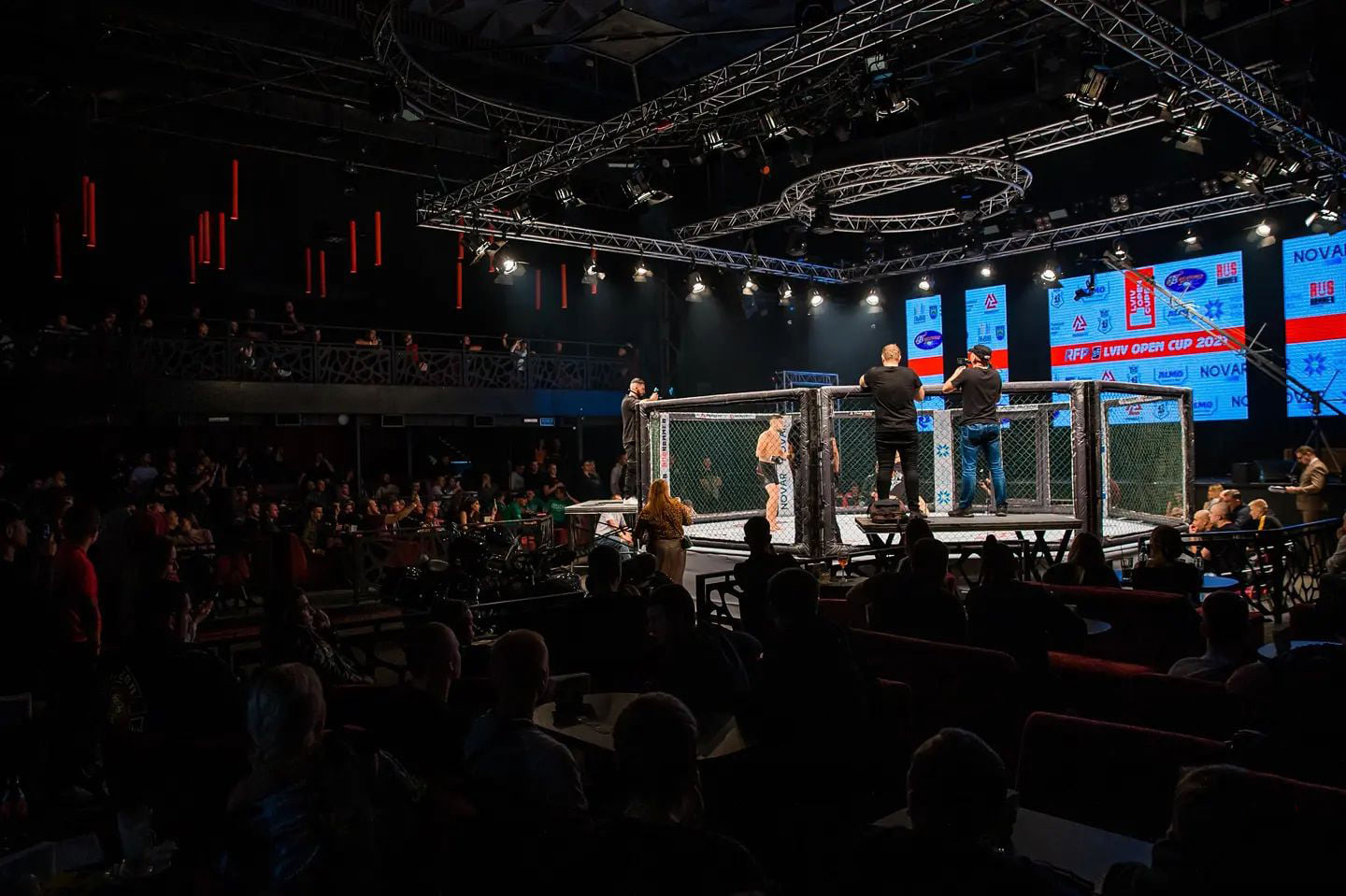 A panoramic view of an MMA event with the lit cage and audience.