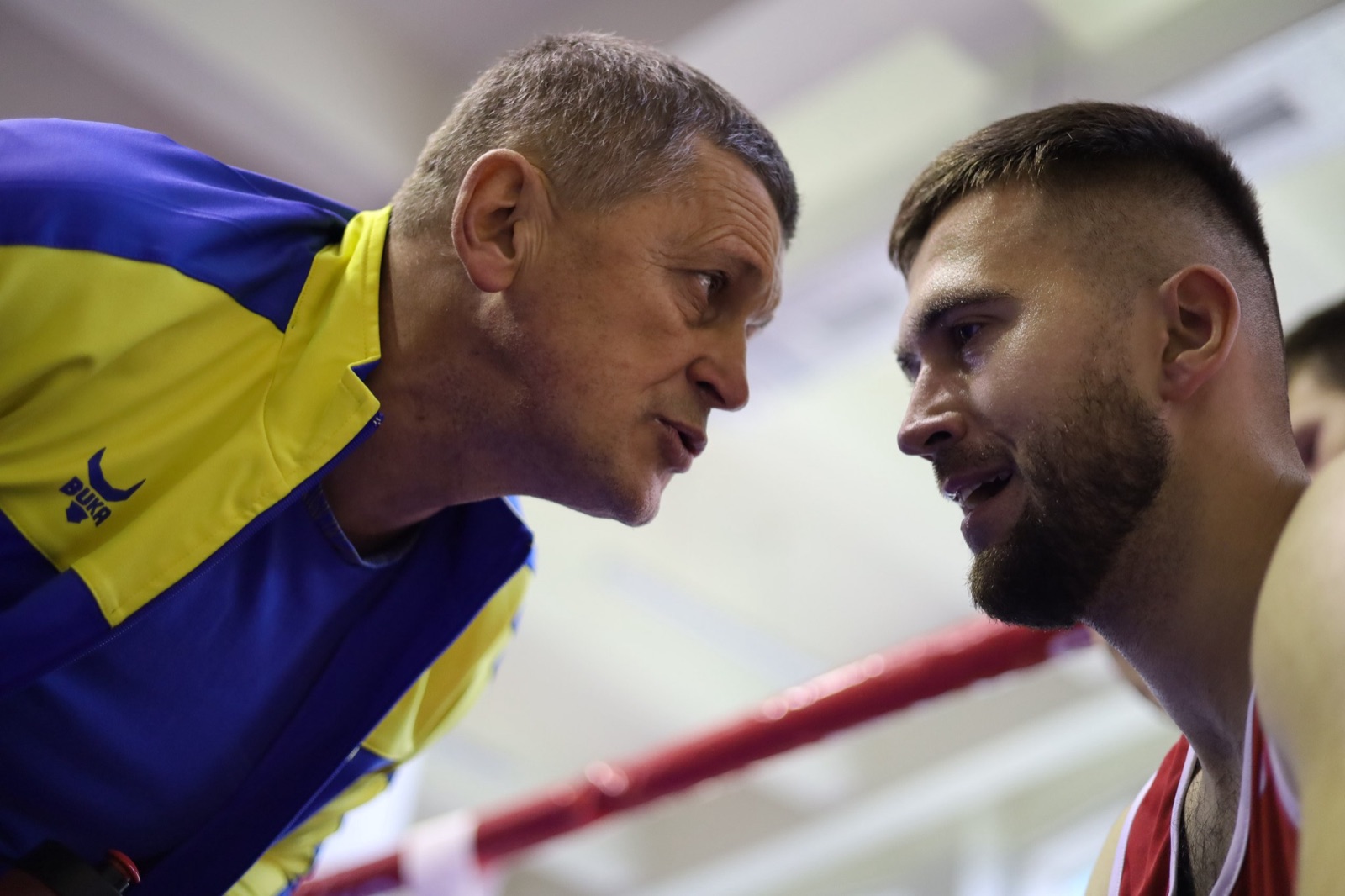 A coach and fighter share a moment beside the Ukrainian flag.